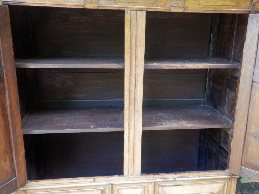 An 18th-century solid oak hall cupboard featuring double doors with geometric fielded panelling, lower drawers, and a stepped top cornice. View X