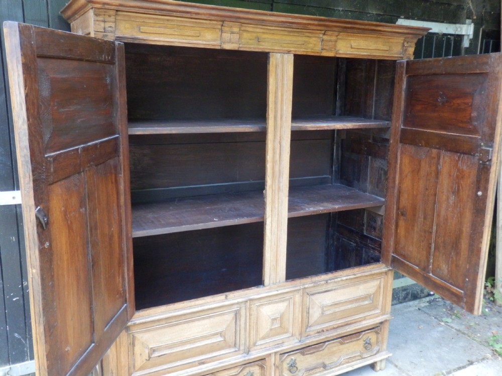 An 18th-century solid oak hall cupboard featuring double doors with geometric fielded panelling, lower drawers, and a stepped top cornice. View XI