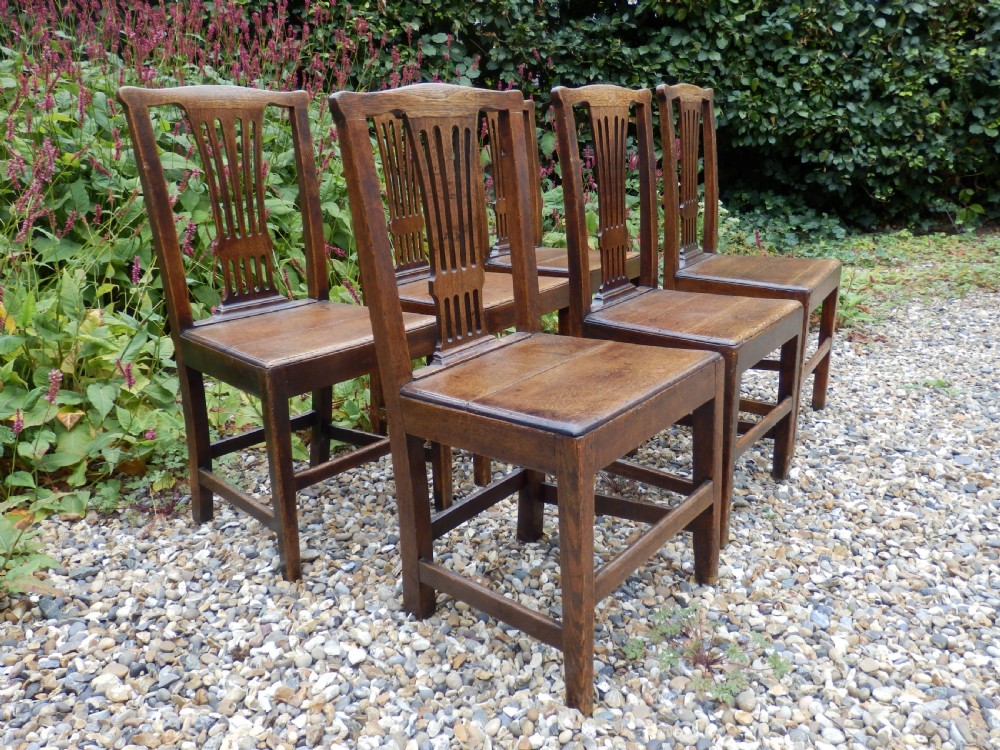 A set of six dark oak Georgian dining chairs featuring pierced vertical back splats, solid wooden seats, and straight legs connected by stretchers.