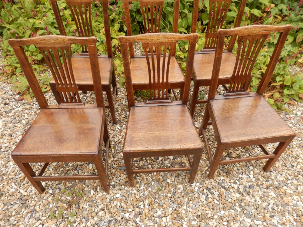 A set of six dark oak Georgian dining chairs featuring pierced vertical back splats, solid wooden seats, and straight legs connected by stretchers. View VI