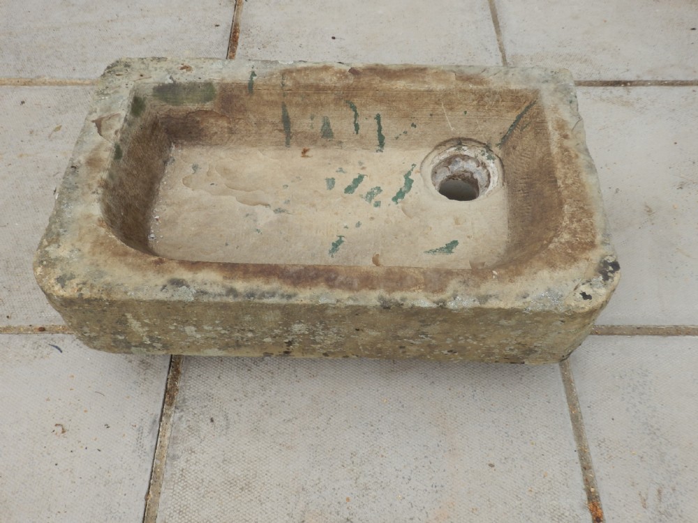 A rectangular, hand-carved antique stone sink displaying a textured exterior, weathered patina, and a corner drainage hole. View III