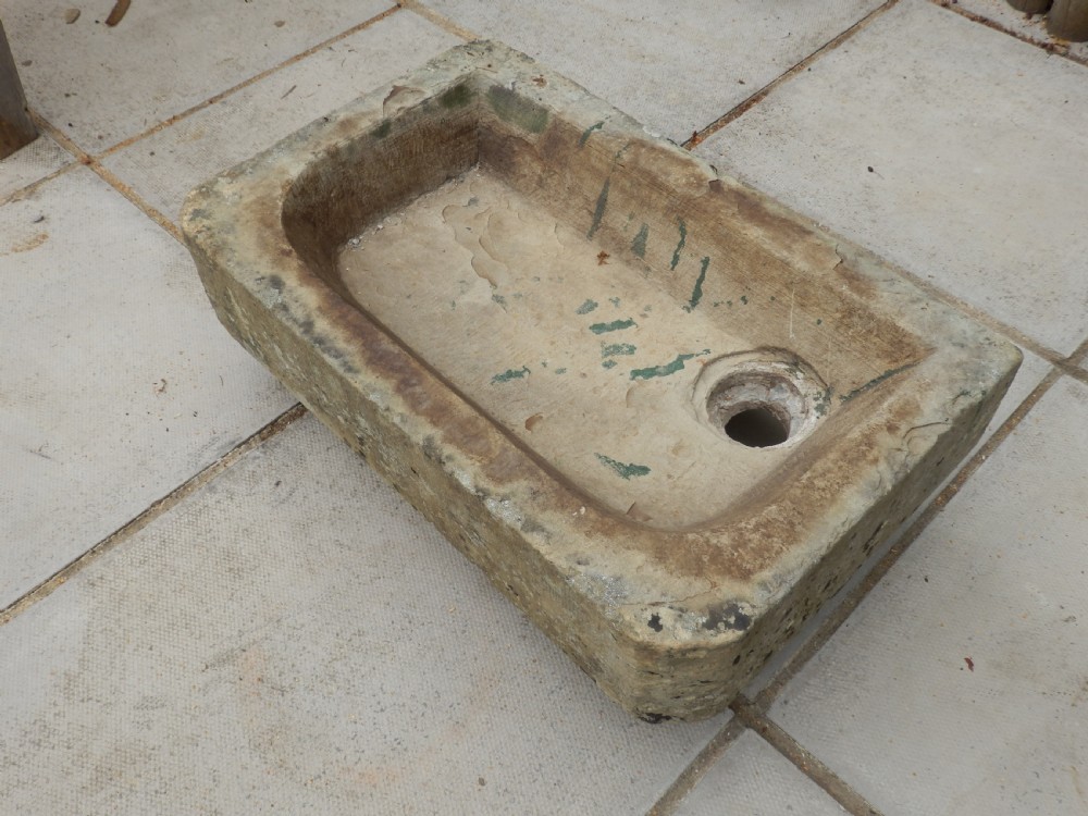 A rectangular, hand-carved antique stone sink displaying a textured exterior, weathered patina, and a corner drainage hole. View IV