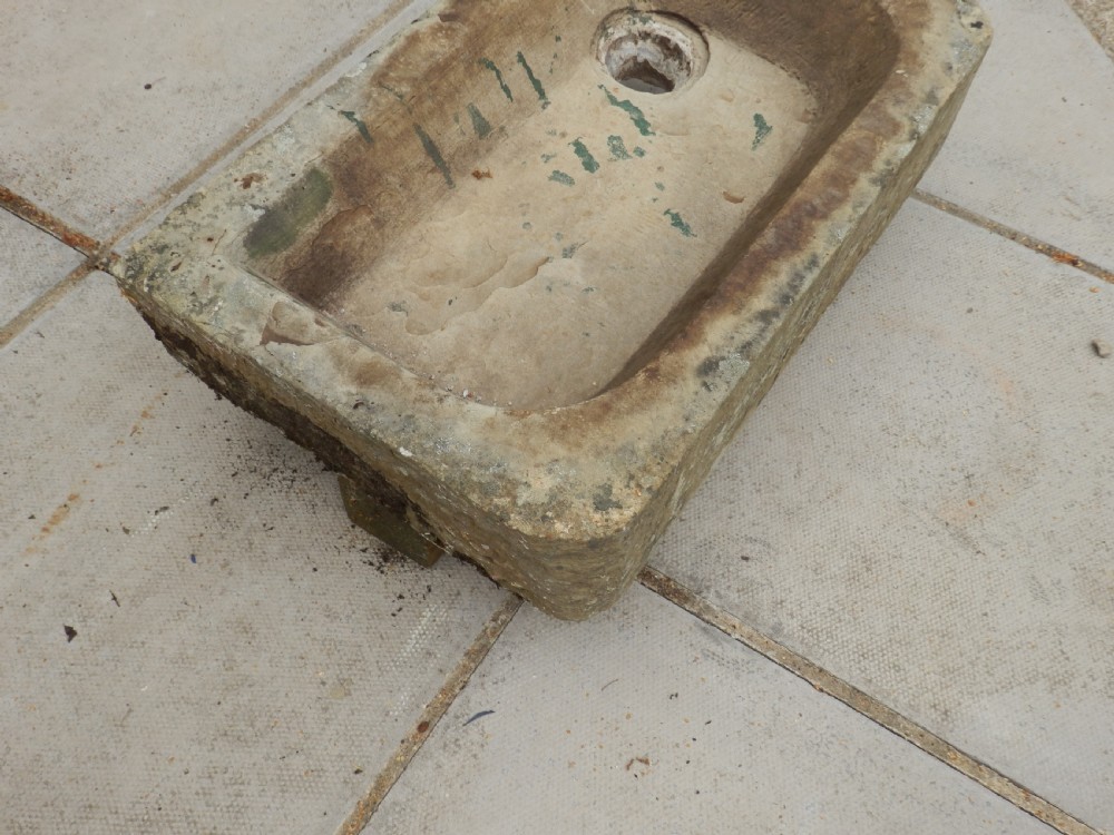 A rectangular, hand-carved antique stone sink displaying a textured exterior, weathered patina, and a corner drainage hole. View V