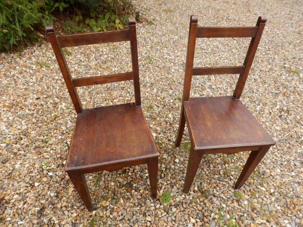 A pair of antique dark oak dining chairs with flat horizontal back slats, solid wood seats, and straight legs.