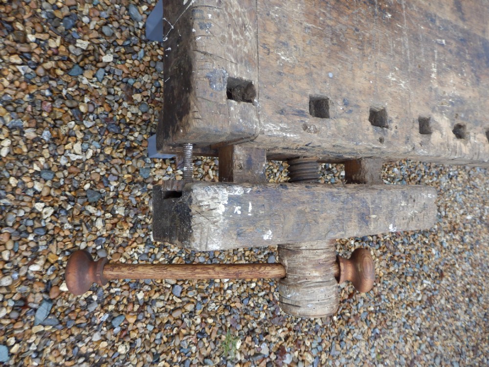 An antique wooden carpenters workbench featuring a thick weathered timber top with integrated vices on a painted grey base. View VI