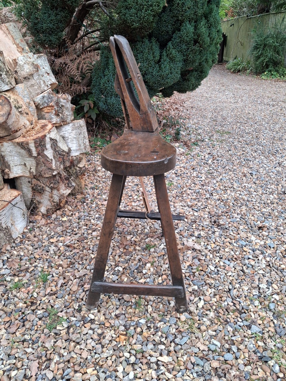 A dark timber saddlers stitching pony bench featuring an upright wooden clamp mounted to a four-legged stool base.