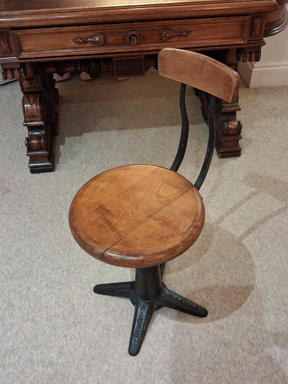 An antique Singer machinist stool featuring a black cast iron four-legged base, a round wooden seat, and a curved wooden backrest.