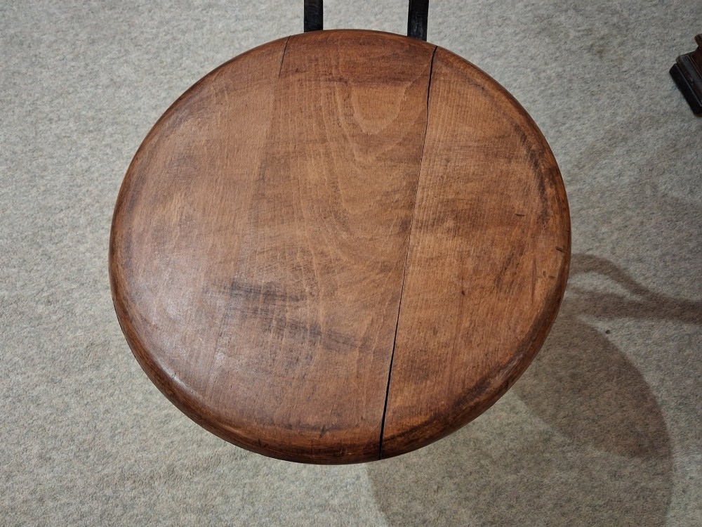 An antique Singer machinist stool featuring a black cast iron four-legged base, a round wooden seat, and a curved wooden backrest. View II
