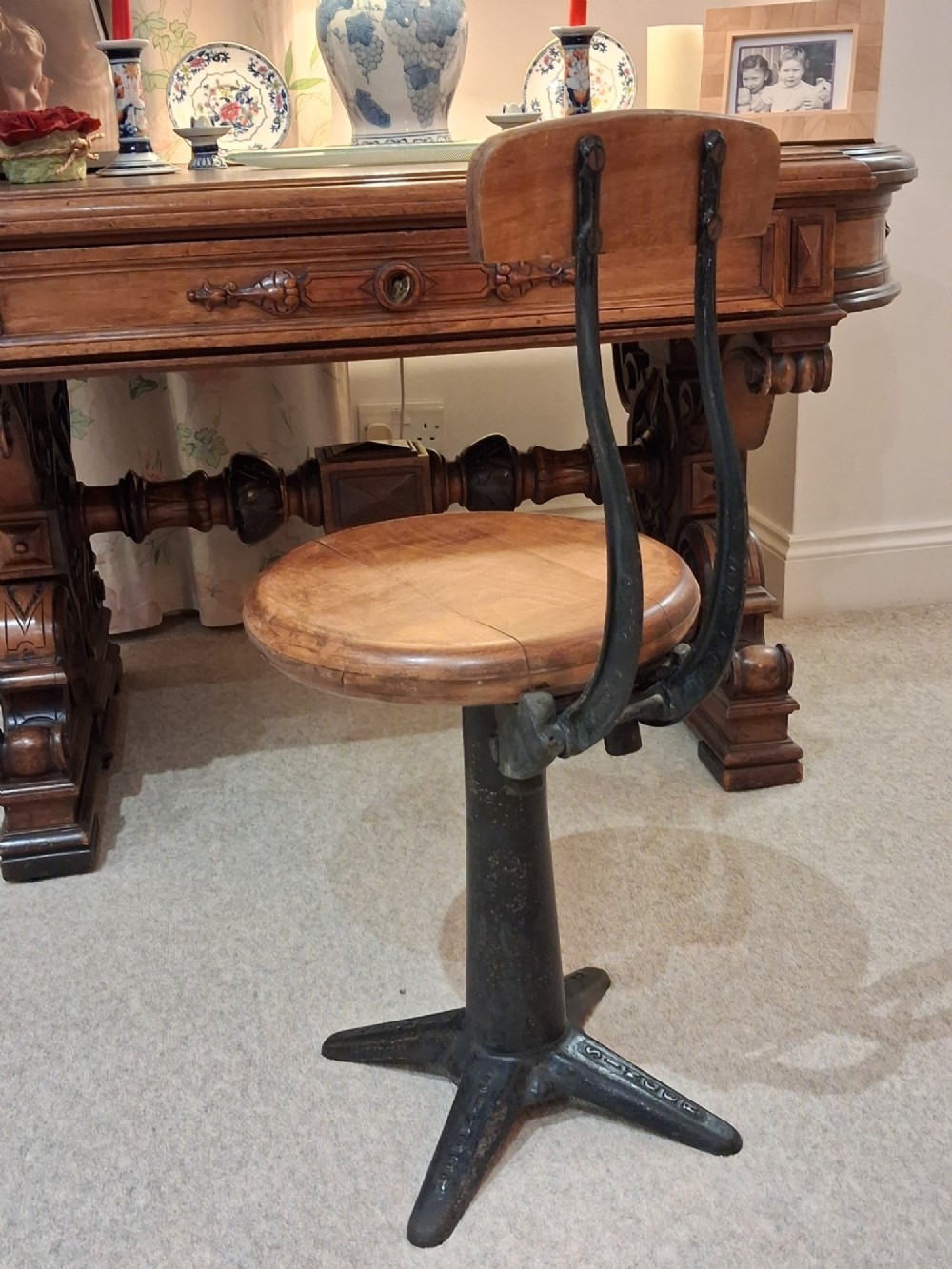 An antique Singer machinist stool featuring a black cast iron four-legged base, a round wooden seat, and a curved wooden backrest. View III