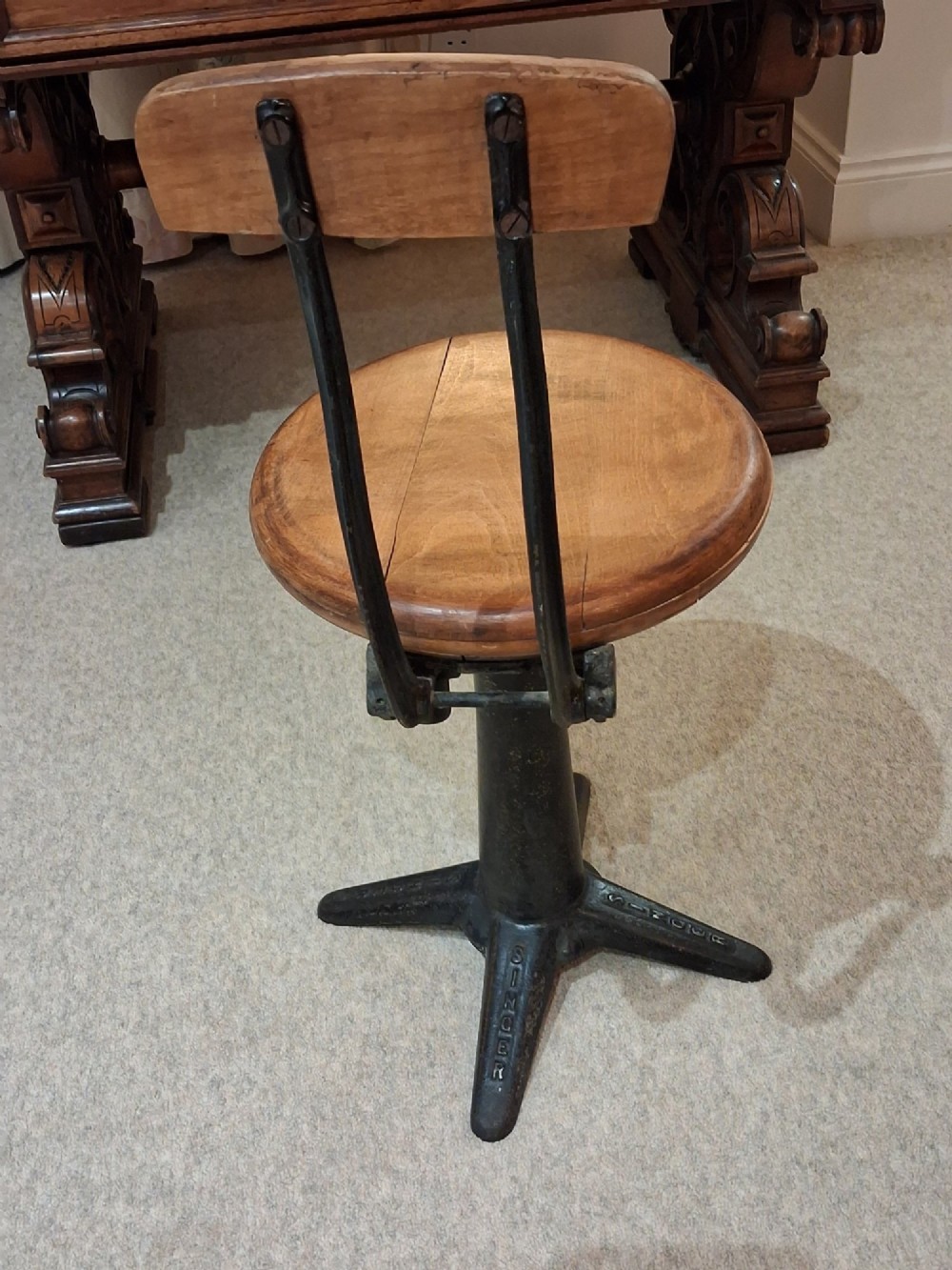 An antique Singer machinist stool featuring a black cast iron four-legged base, a round wooden seat, and a curved wooden backrest. View IV