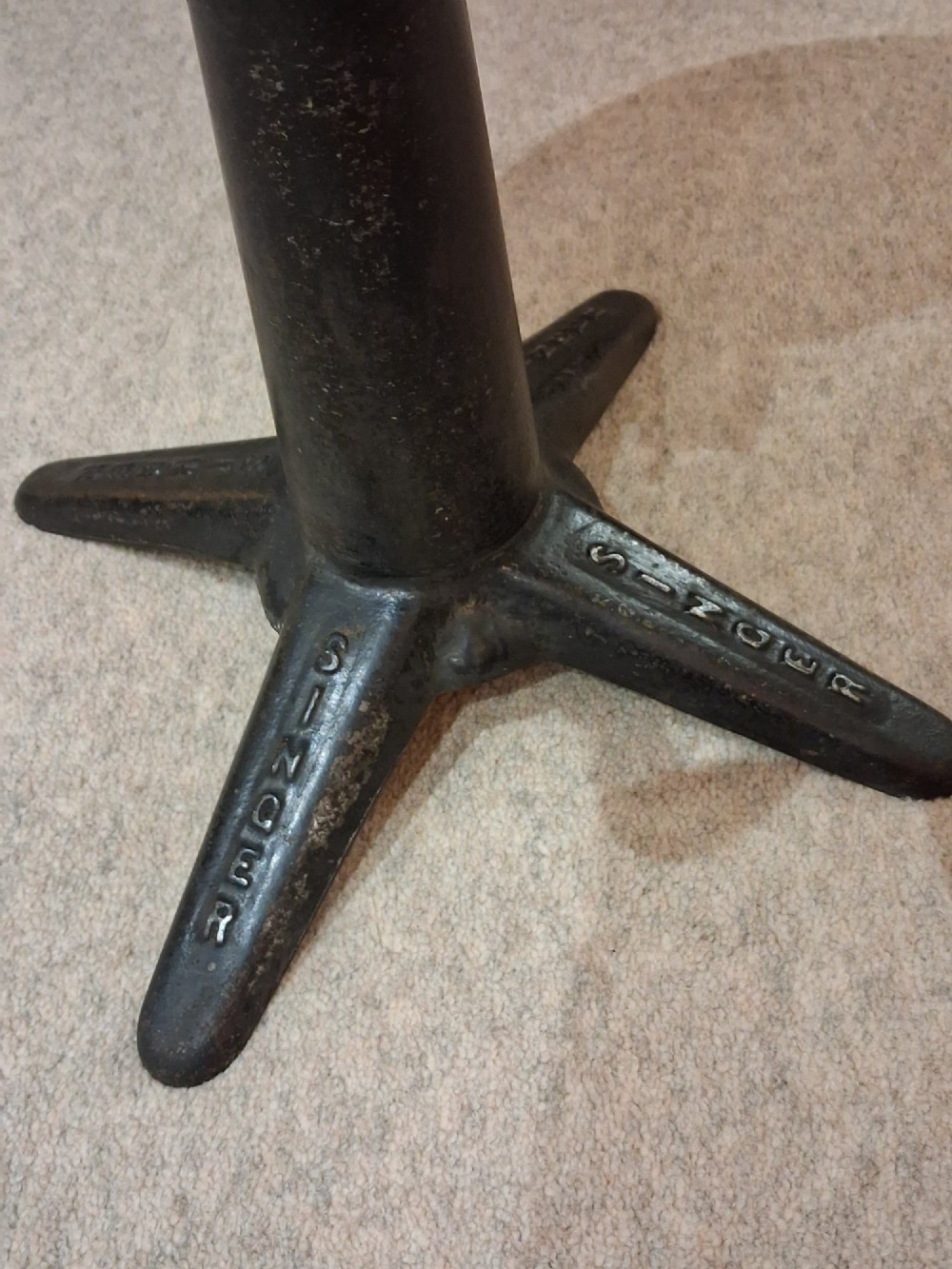 An antique Singer machinist stool featuring a black cast iron four-legged base, a round wooden seat, and a curved wooden backrest. View V