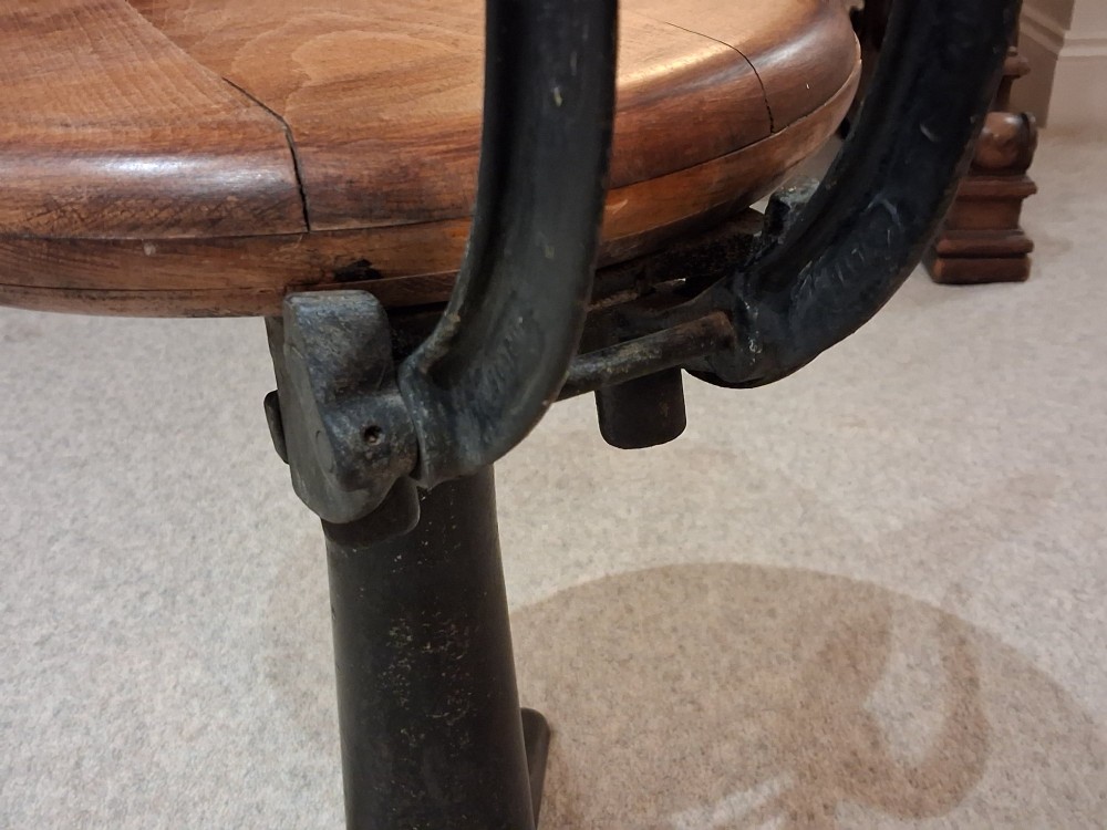 An antique Singer machinist stool featuring a black cast iron four-legged base, a round wooden seat, and a curved wooden backrest. View VI