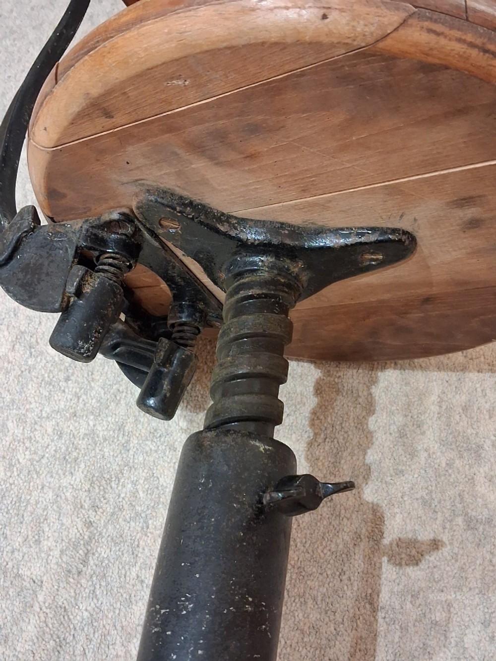 An antique Singer machinist stool featuring a black cast iron four-legged base, a round wooden seat, and a curved wooden backrest. View VII