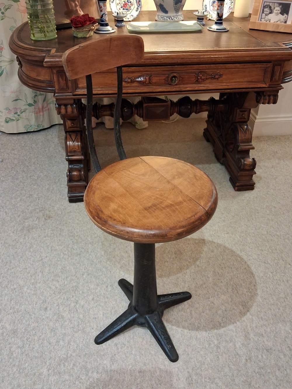 An antique Singer machinist stool featuring a black cast iron four-legged base, a round wooden seat, and a curved wooden backrest. View VIII