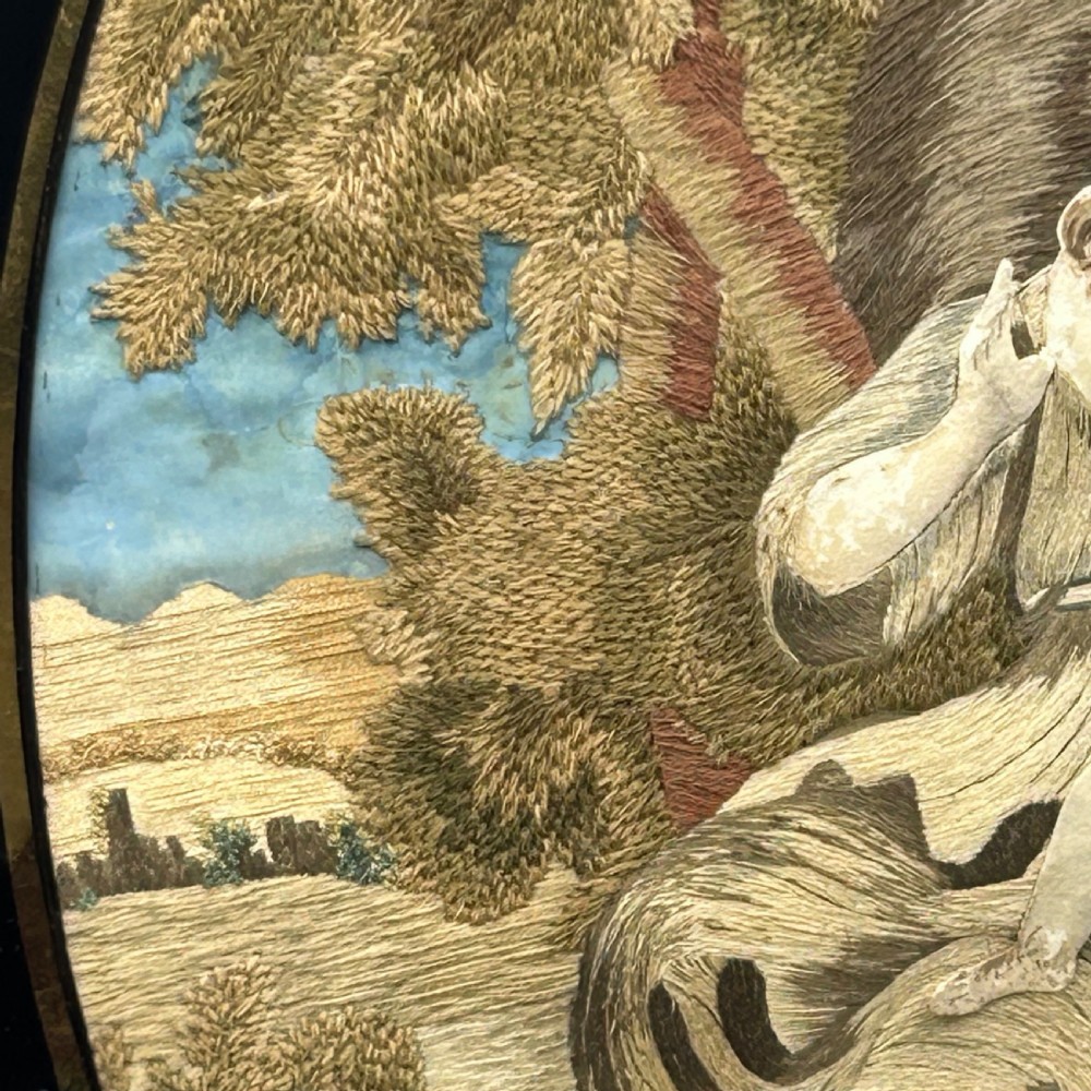 An oval Georgian silk embroidery depicting a seated woman and child within a landscape, featuring painted paper faces and set in a black frame. View IV