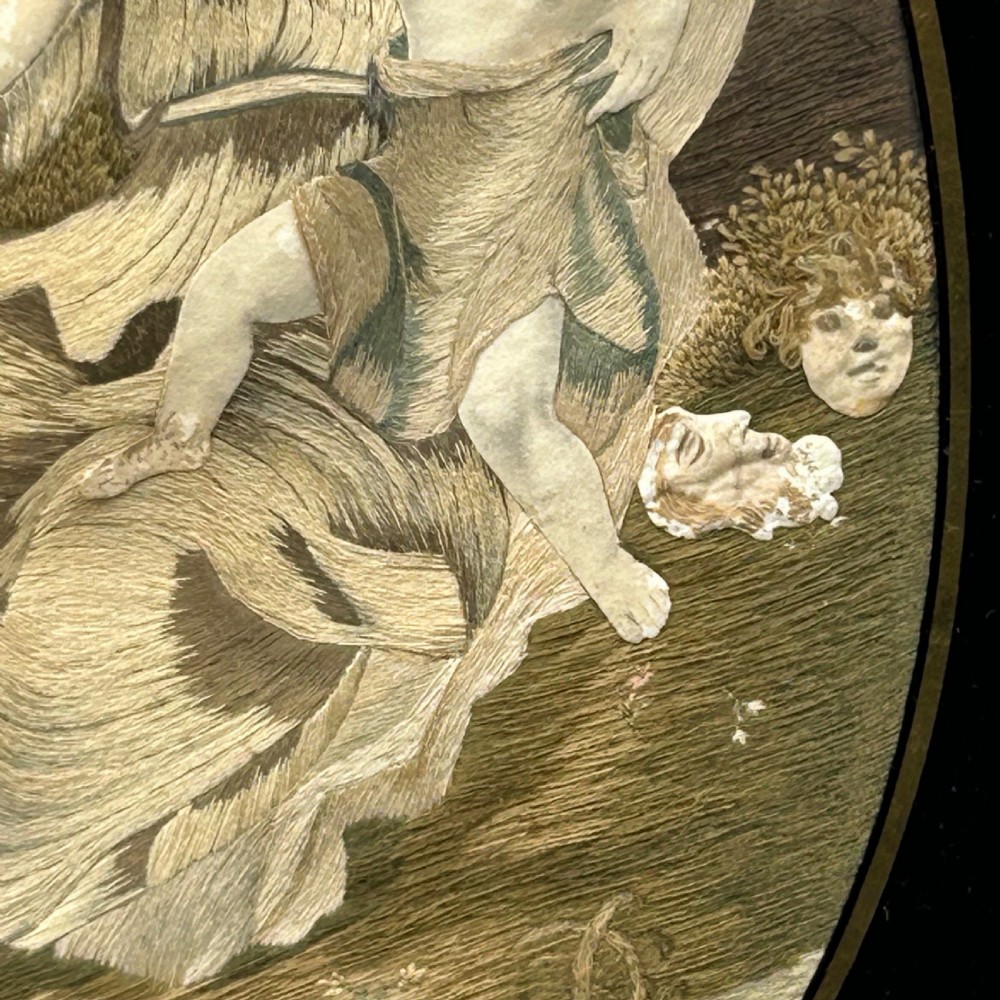 An oval Georgian silk embroidery depicting a seated woman and child within a landscape, featuring painted paper faces and set in a black frame. View VIII