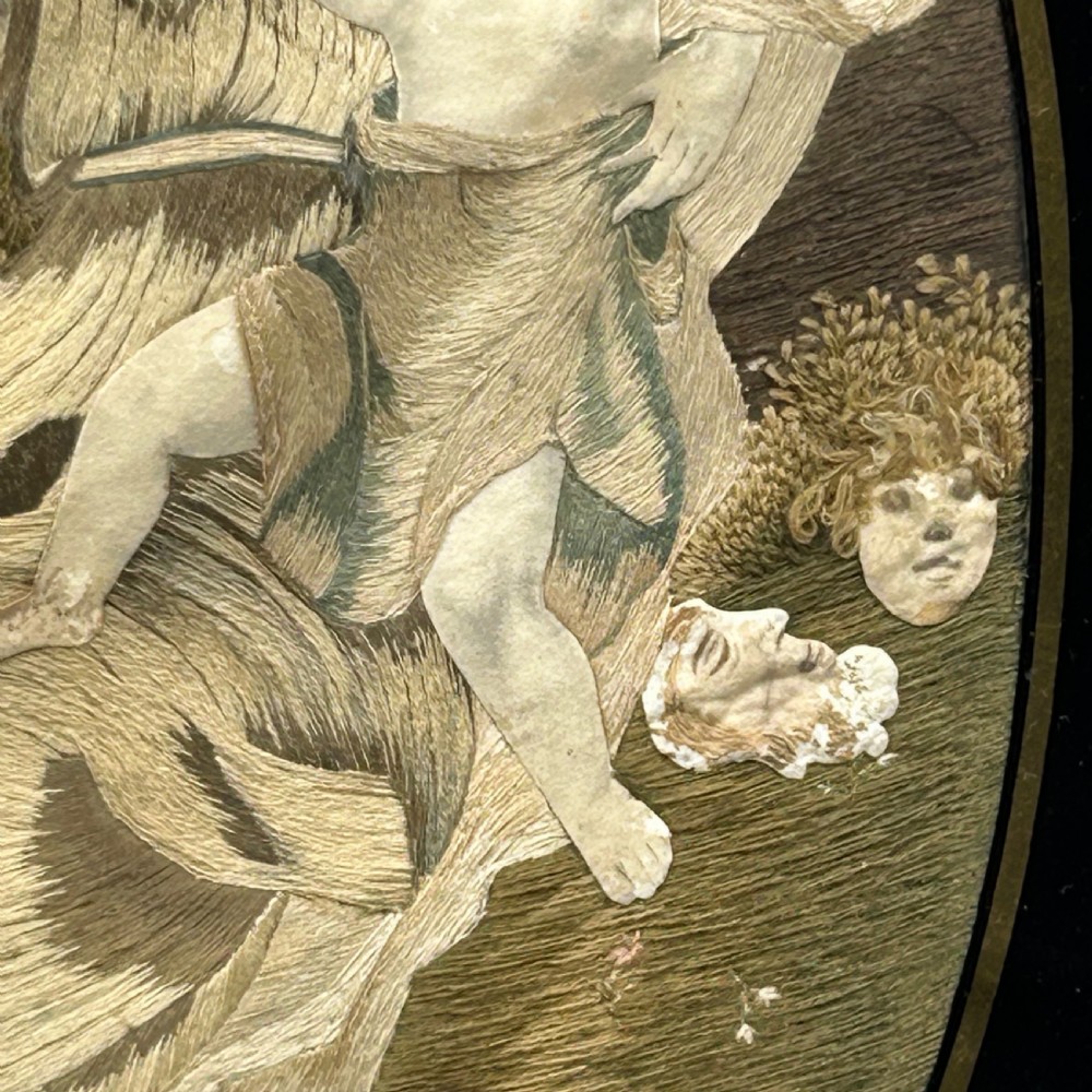 An oval Georgian silk embroidery depicting a seated woman and child within a landscape, featuring painted paper faces and set in a black frame. View XI
