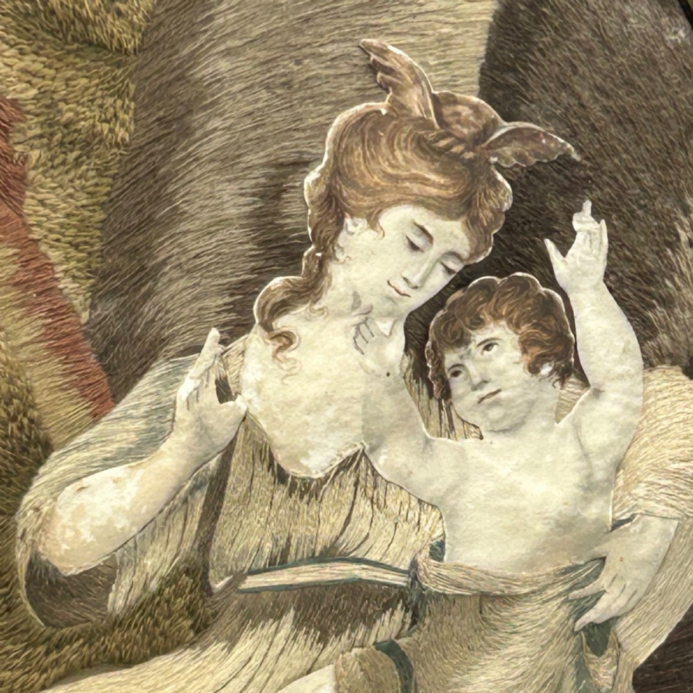 An oval Georgian silk embroidery depicting a seated woman and child within a landscape, featuring painted paper faces and set in a black frame. View XIII
