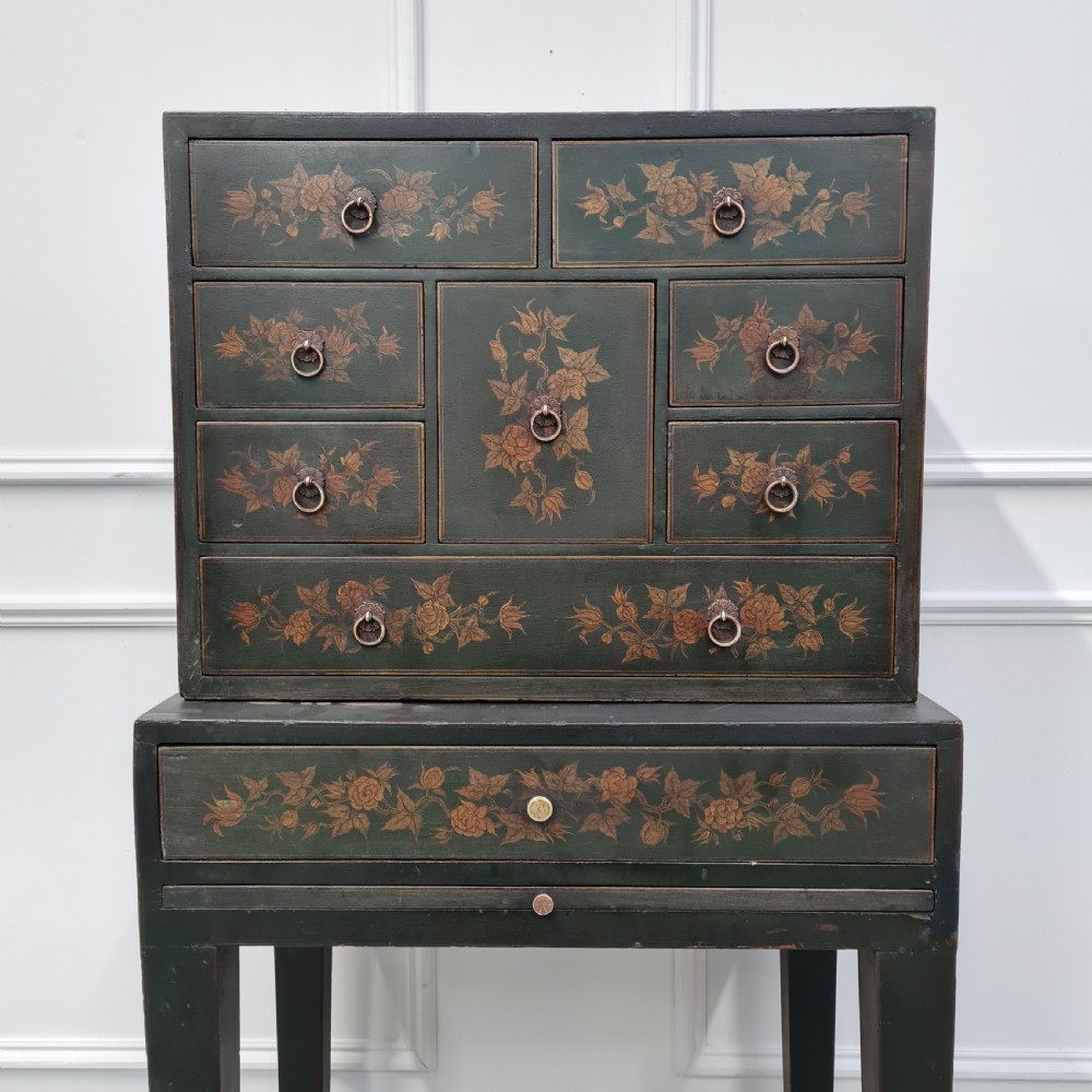 A dark green late Victorian collectors cabinet on a tall stand, featuring hand-painted floral motifs, multiple drawers, and brass ring handles. View II