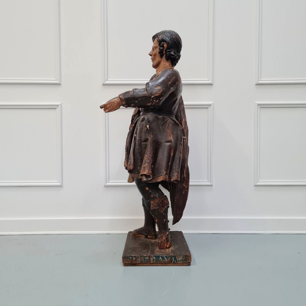 Full-length carved wood polychrome figure of a standing man in 17th-century attire on an inscribed rectangular base. View X