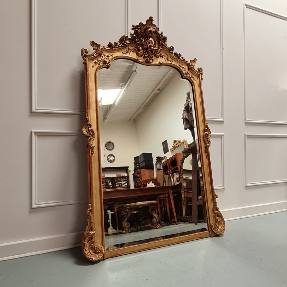 Large French 19th century arched mirror featuring a gilded frame with ornate Rococo cresting and detailed corner scrollwork.