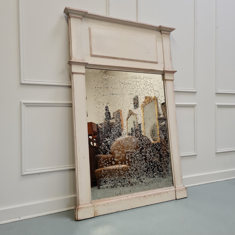 An antique French painted wood trumeau mirror featuring a rectangular frame with architectural mouldings and heavily foxed mirror glass.
