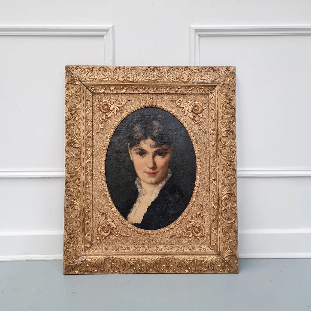 A 19th-century French oil painting depicting a dark-haired woman set within an oval spandrel inside an ornate rectangular gold gilt frame.