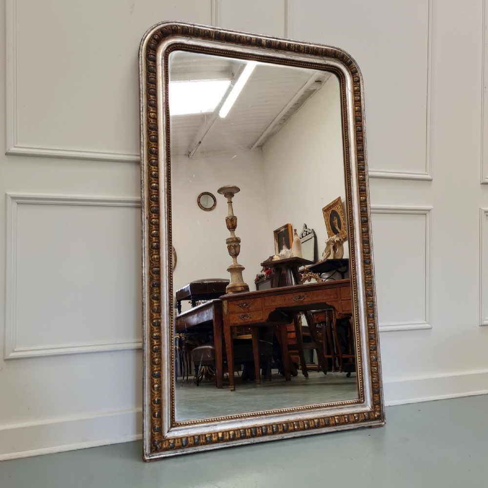 A large French antique mirror featuring a silver leaf frame with rounded upper corners and beaded moulding.