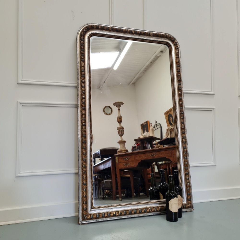A large French antique mirror featuring a silver leaf frame with rounded upper corners and beaded moulding. View VII