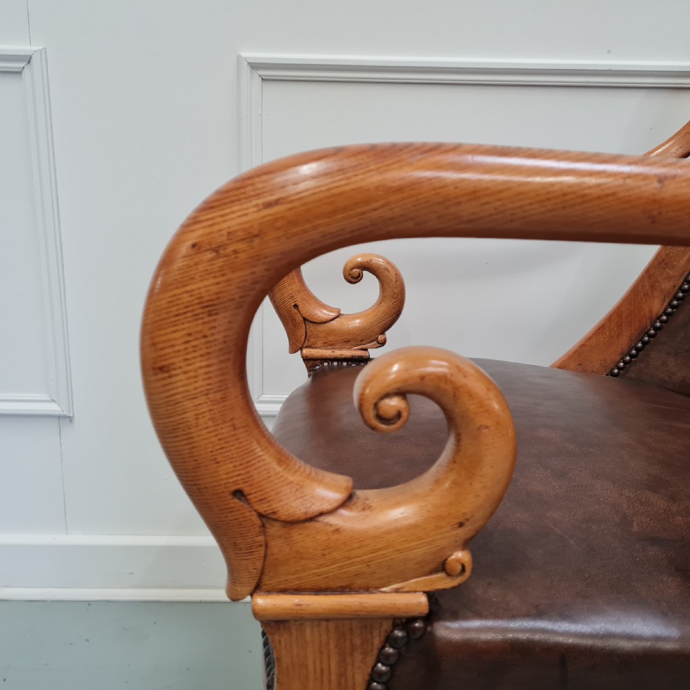 Pair of mid-19th-century ash wood armchairs featuring brown leather upholstery, stud detailing, and carved scrolled armrests. View V