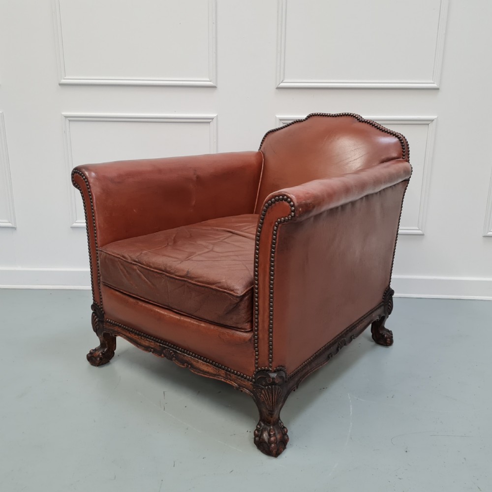 A 1930s brown leather armchair featuring brass studding trim and carved wooden feet.