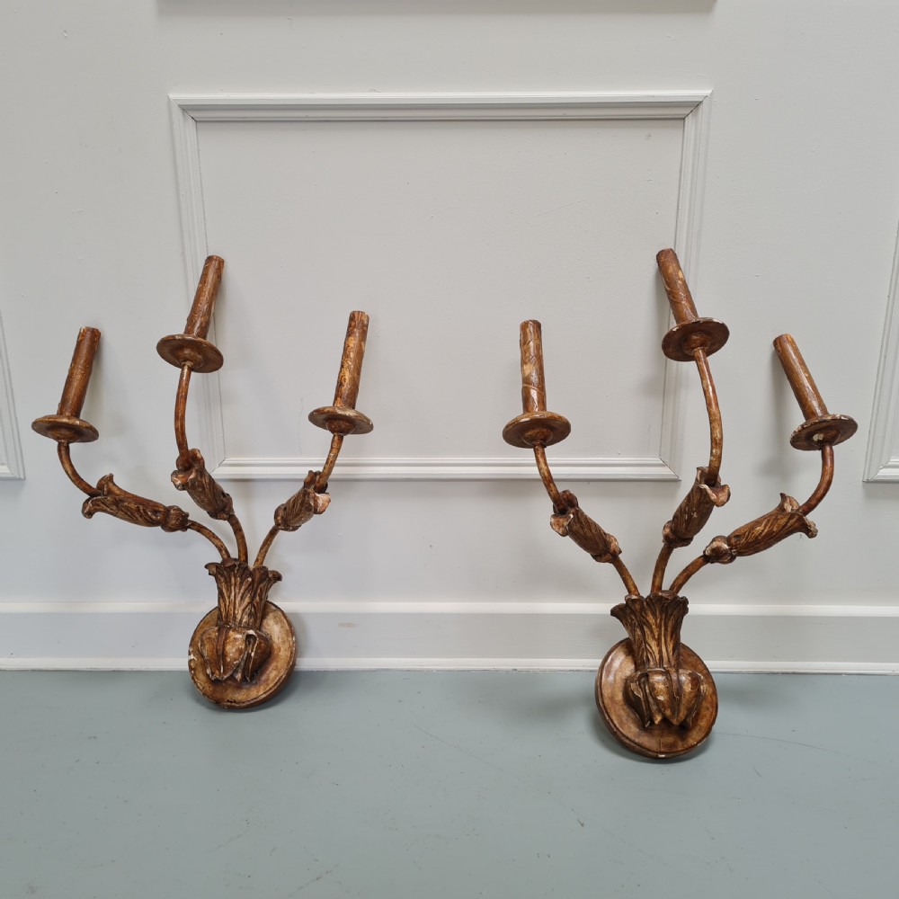 A pair of late 18th-century carved giltwood three-arm wall lights with foliate bases and slender curved arms.