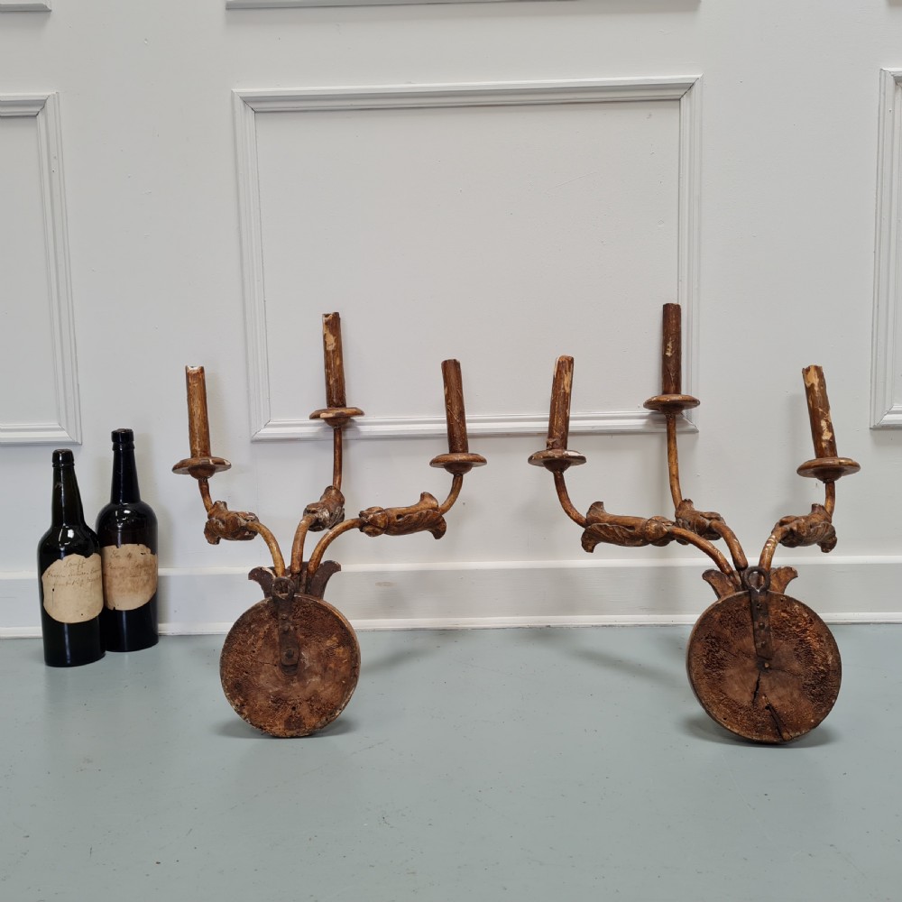 A pair of late 18th-century carved giltwood three-arm wall lights with foliate bases and slender curved arms. View V