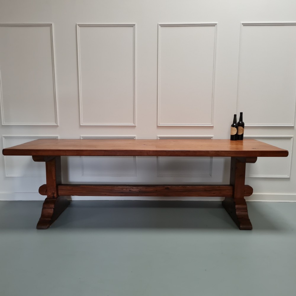 A large, solid warm brown oak monastery dining table featuring a thick rectangular top supported by robust end trestles and a low central stretcher rail. View II