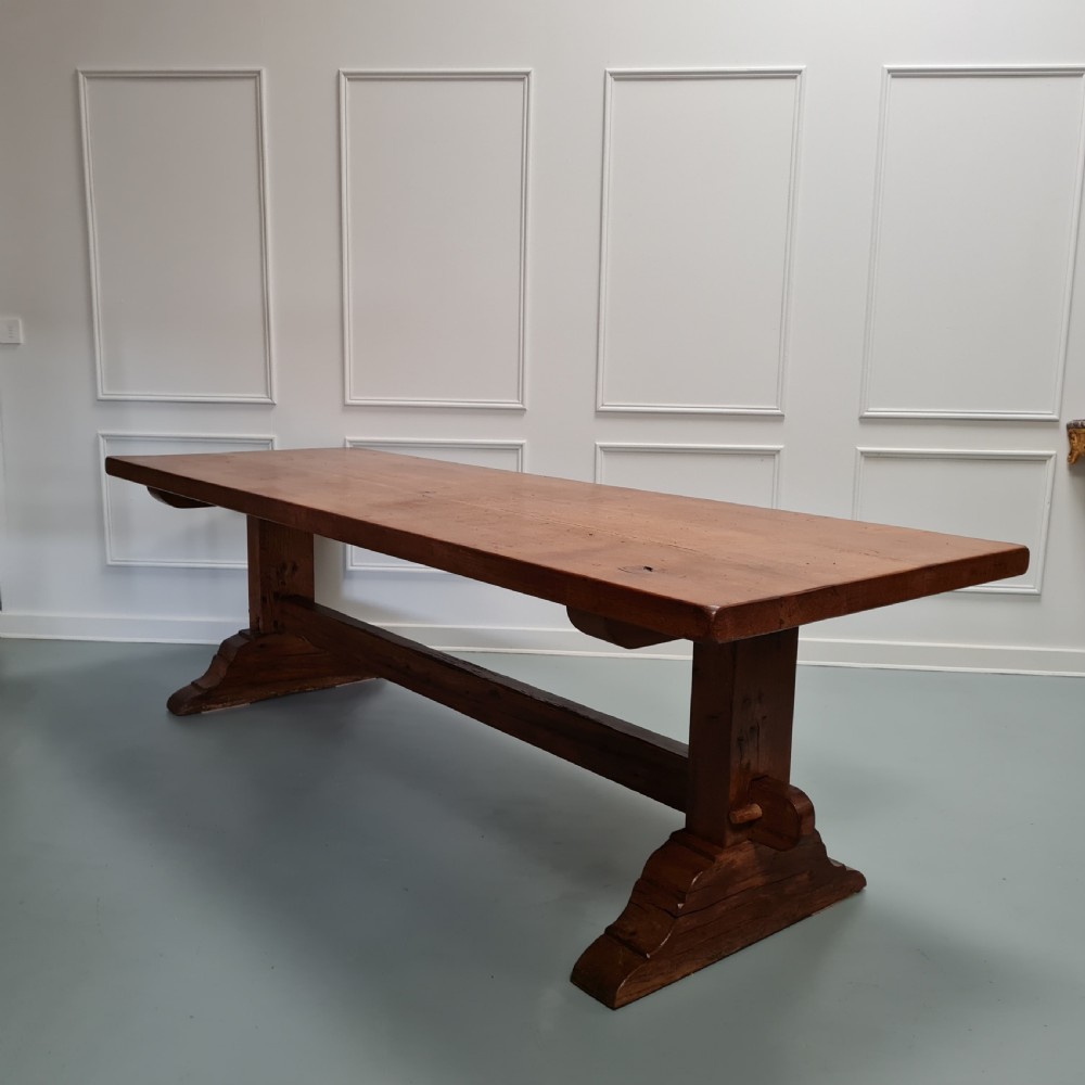 A large, solid warm brown oak monastery dining table featuring a thick rectangular top supported by robust end trestles and a low central stretcher rail. View III