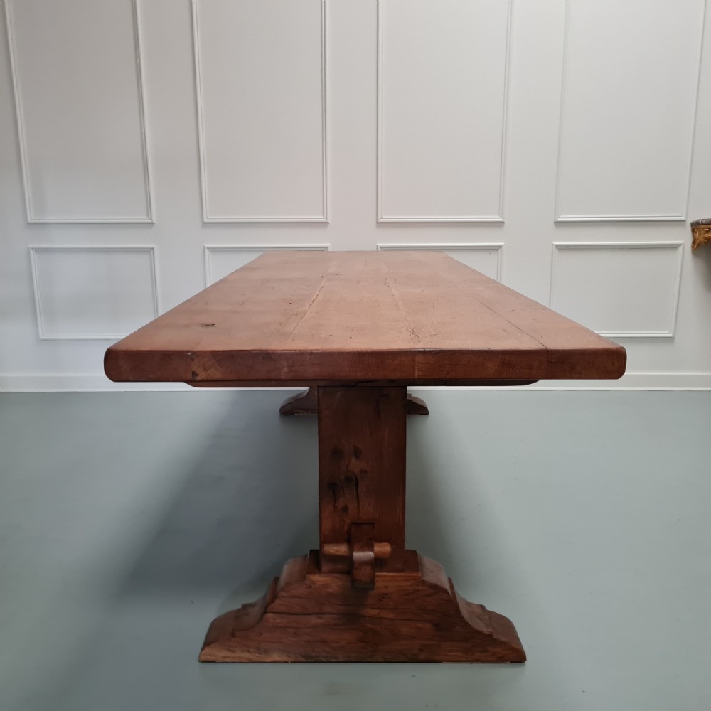 A large, solid warm brown oak monastery dining table featuring a thick rectangular top supported by robust end trestles and a low central stretcher rail. View IV