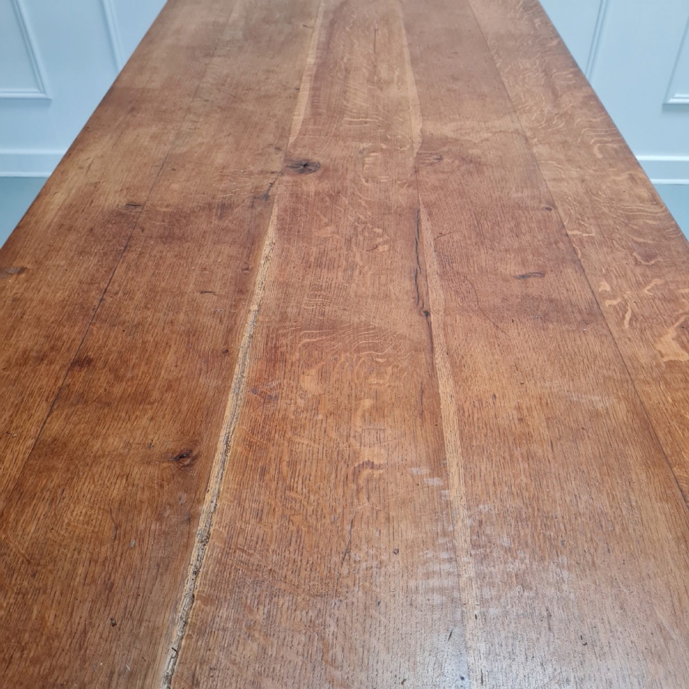 A large, solid warm brown oak monastery dining table featuring a thick rectangular top supported by robust end trestles and a low central stretcher rail. View V