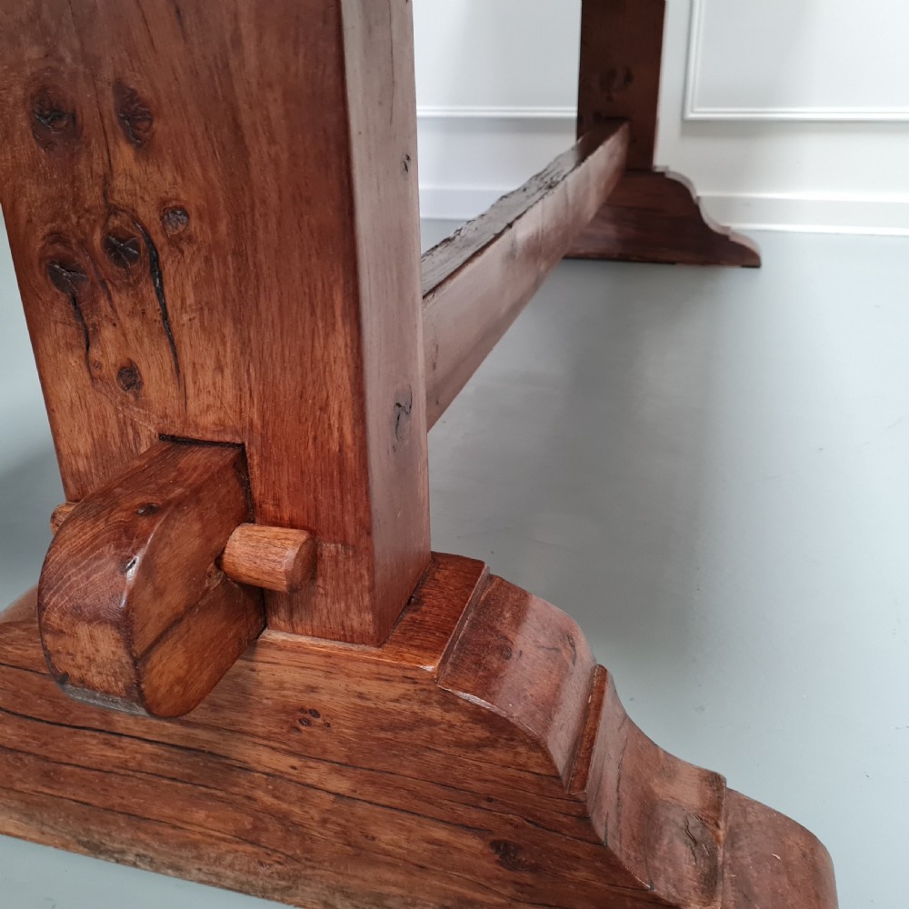 A large, solid warm brown oak monastery dining table featuring a thick rectangular top supported by robust end trestles and a low central stretcher rail. View VI