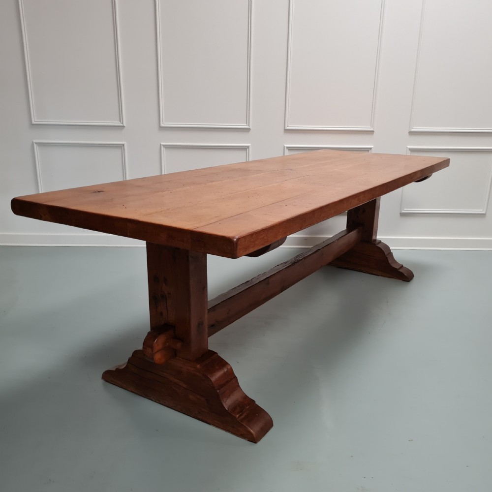 A large, solid warm brown oak monastery dining table featuring a thick rectangular top supported by robust end trestles and a low central stretcher rail. View VII