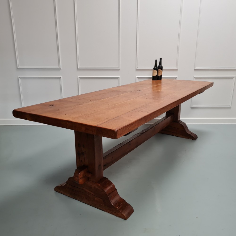 A large, solid warm brown oak monastery dining table featuring a thick rectangular top supported by robust end trestles and a low central stretcher rail. View VIII
