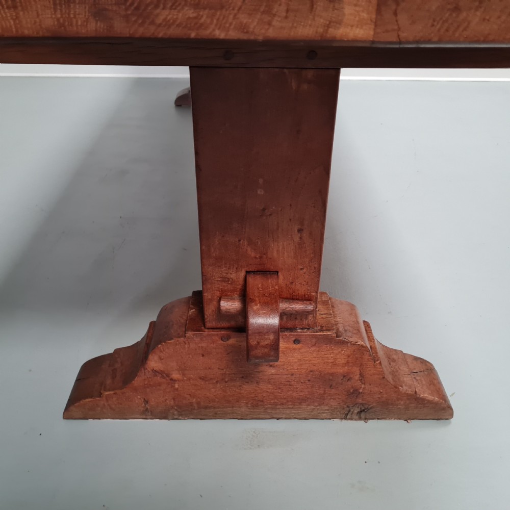 A large, solid warm brown oak monastery dining table featuring a thick rectangular top supported by robust end trestles and a low central stretcher rail. View IX