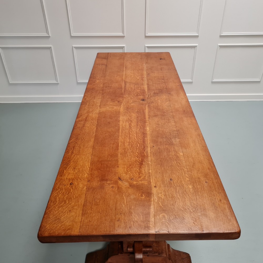 A large, solid warm brown oak monastery dining table featuring a thick rectangular top supported by robust end trestles and a low central stretcher rail. View X