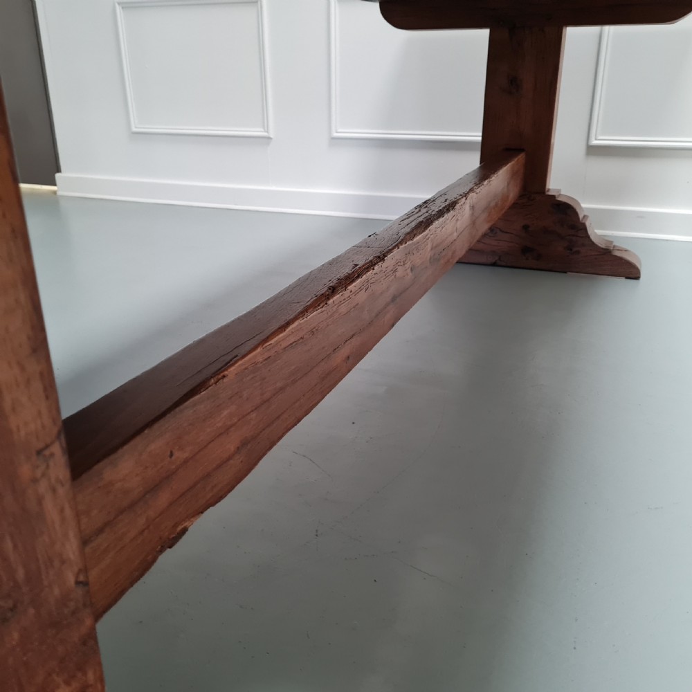 A large, solid warm brown oak monastery dining table featuring a thick rectangular top supported by robust end trestles and a low central stretcher rail. View XI