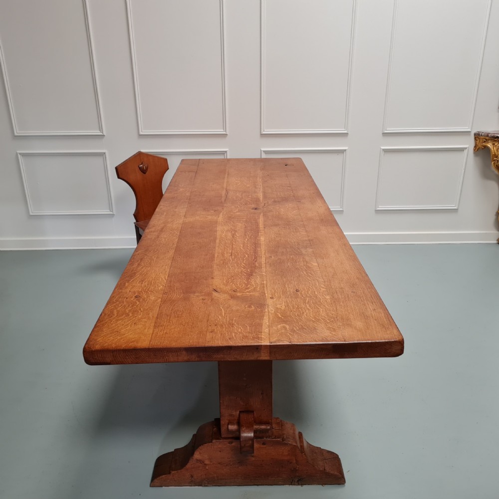A large, solid warm brown oak monastery dining table featuring a thick rectangular top supported by robust end trestles and a low central stretcher rail. View XII