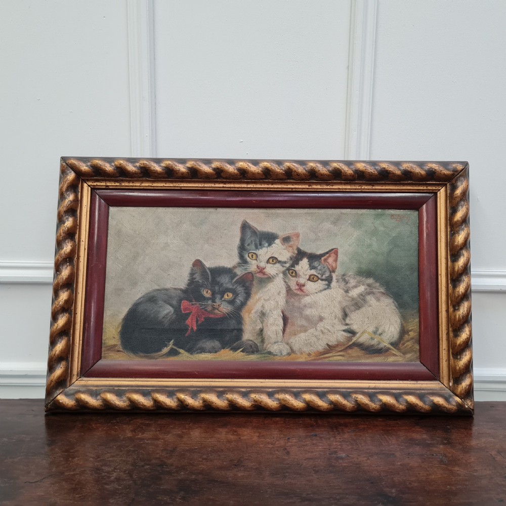 A Victorian oil painting depicting three kittens seated together inside a carved gilded rope-twist wooden frame.