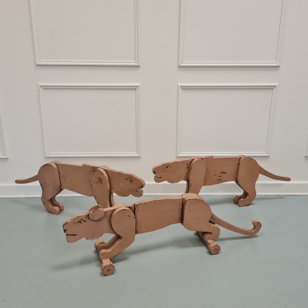 Three articulated painted wooden toy lionesses with small wheels resting on a light surface.