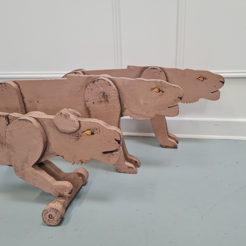 Three articulated painted wooden toy lionesses with small wheels resting on a light surface. View II