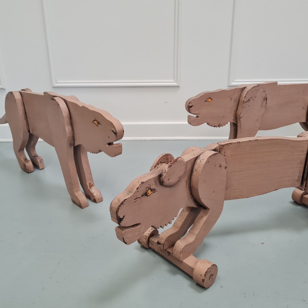 Three articulated painted wooden toy lionesses with small wheels resting on a light surface. View III