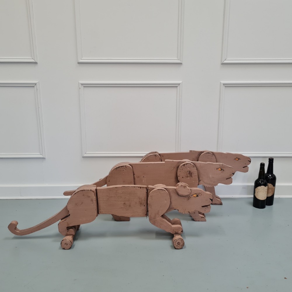Three articulated painted wooden toy lionesses with small wheels resting on a light surface. View VI