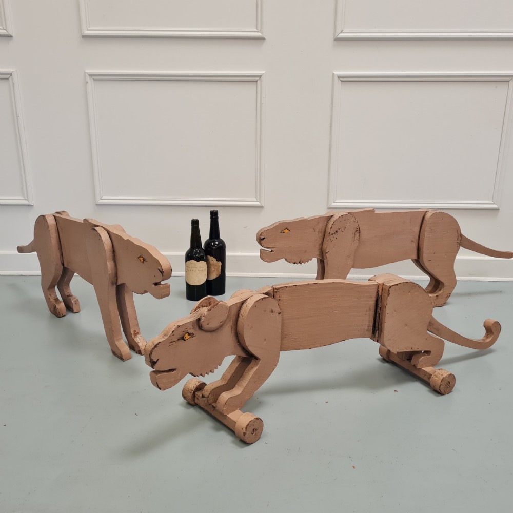 Three articulated painted wooden toy lionesses with small wheels resting on a light surface. View VII